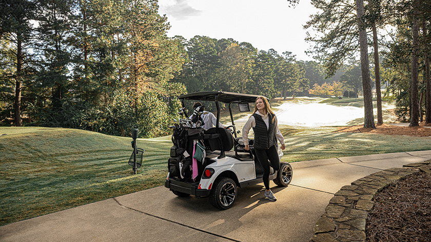 A woman and man getting out of their E-Z-GO golf cart at a golf course.