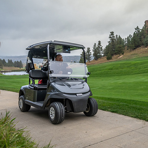 An EX1 E-Z-GO model driving down a golf cart path.