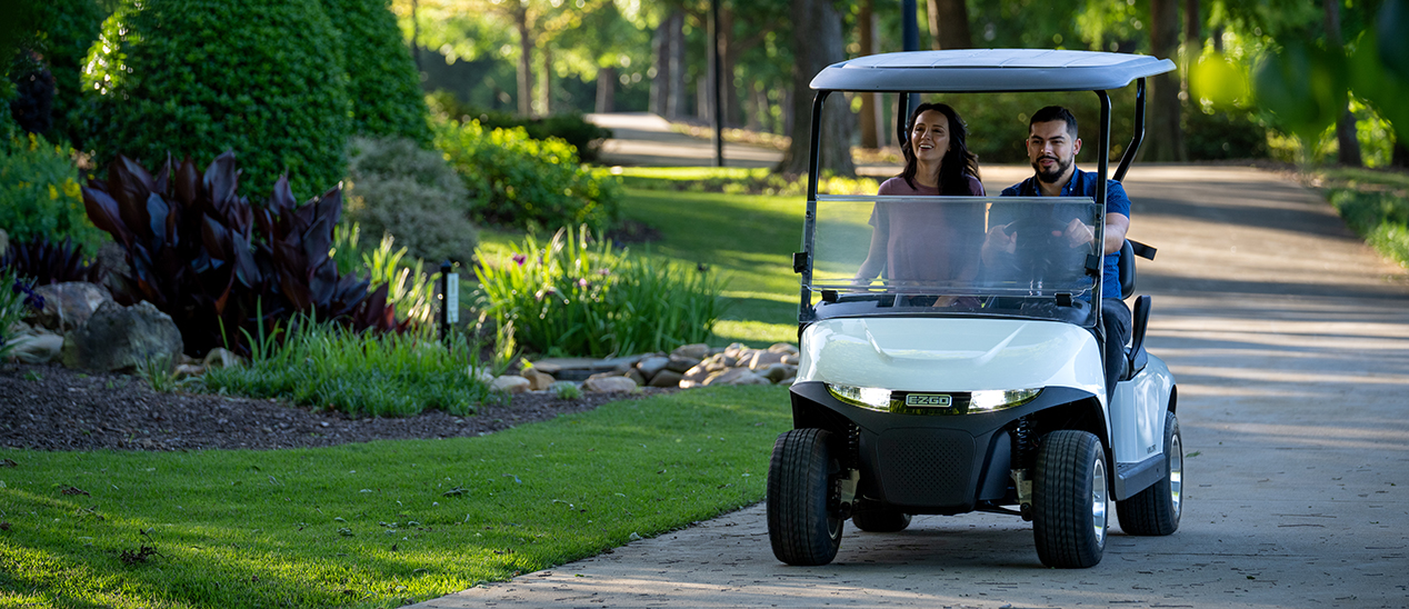 A man and woman drive an E-Z-GO Valor model down an empty path.