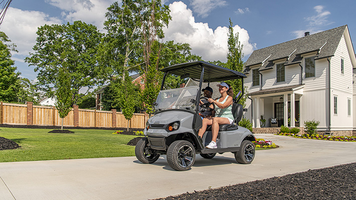 Two people driving an E-Z-GO vehicle in their driveway