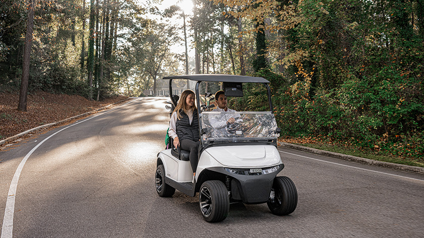 A couple driving an E-Z-GO golf cart down an empty path.