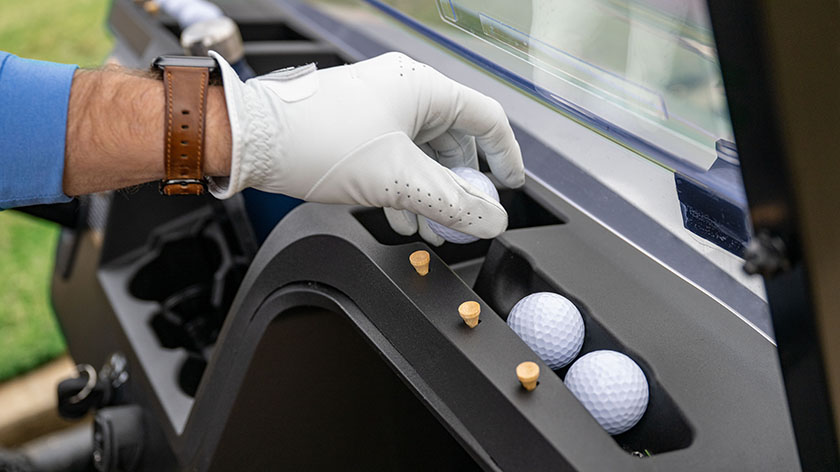 A hand using the golf-centric dash of their E-Z-GO to hold their golf balls and tees.