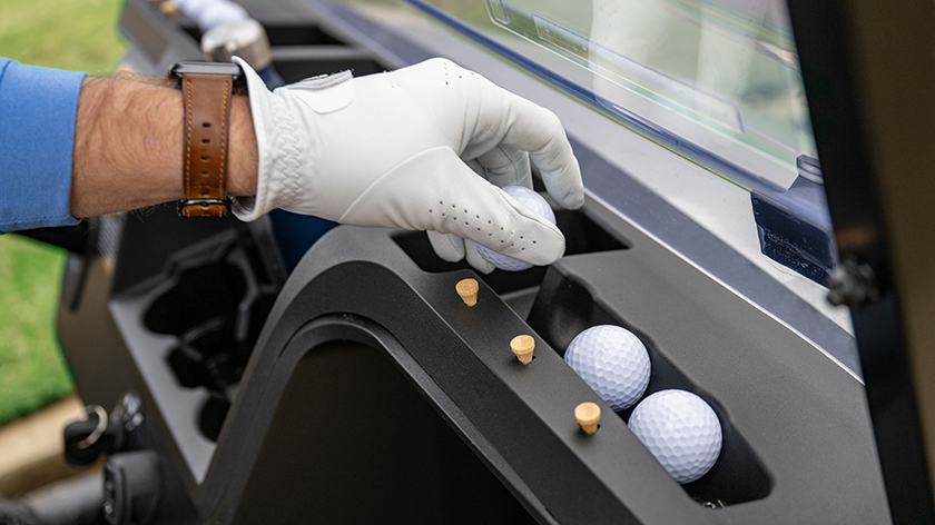 A golfer's hand grabs a golf ball from the golf-centric dash of their E-Z-GO.