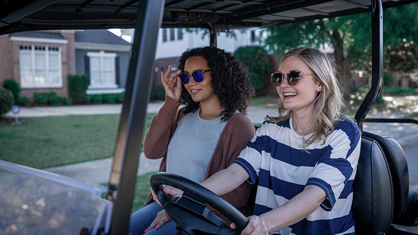 Two women wearing sunglasses while driving an E-Z-GO golf cart.