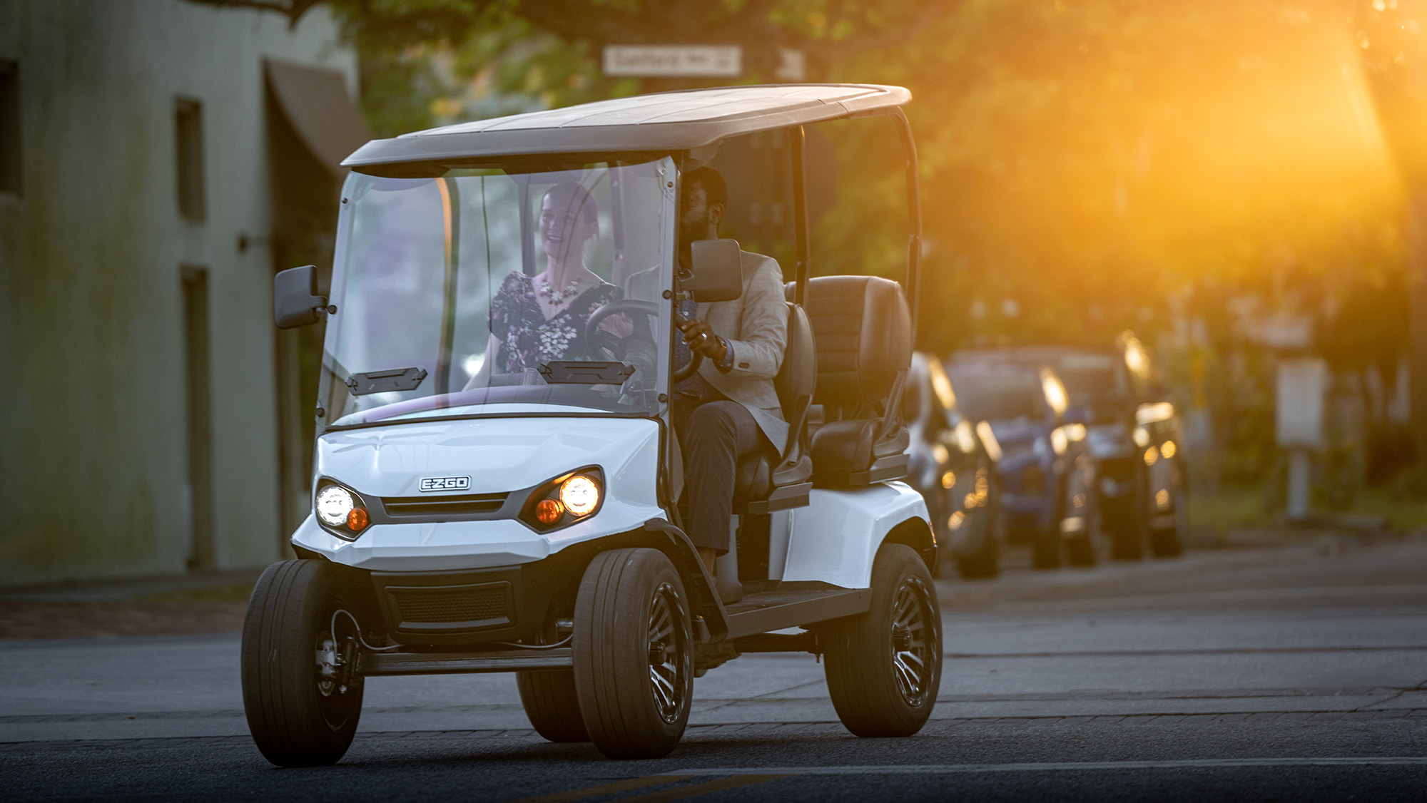 A couple driving an E-Z-GO golf cart down a street.