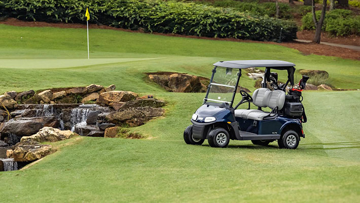An empty E-Z-GO golf cart near a hole on a golf course.