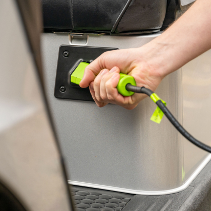 A hand plugs a charger into an E-Z-GO vehicle