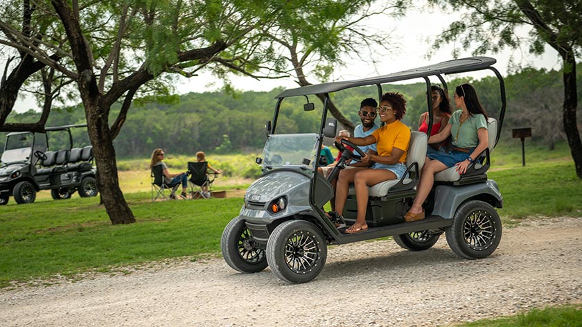 An E-Z-GO Liberty vehicle carrying four passengers on a campground path.