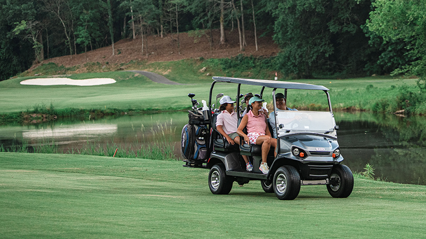 Golfers ride in an E-Z-GO golf cart on a golf course.