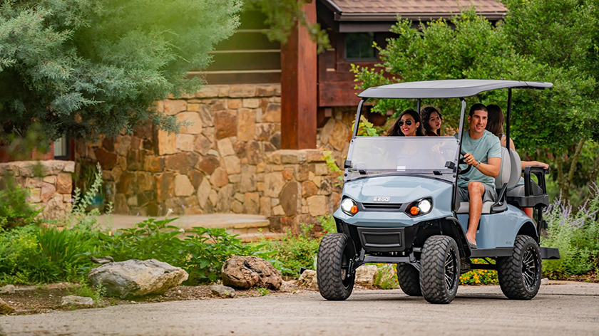 An E-Z-GO vehicle drives toward the camera with greenery surrounding it.