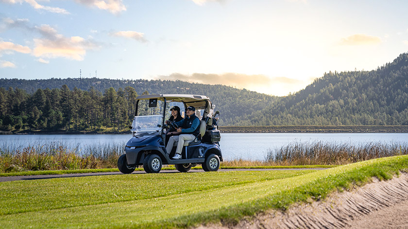 An E-Z-GO golf cart driving down a path with mountains and a sunset in the background.