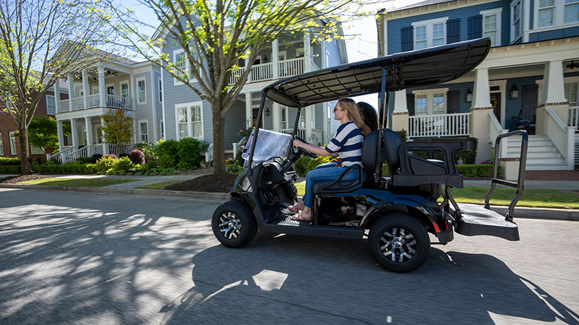 Two women drive an E-Z-GO golf cart down a neighborhood street.