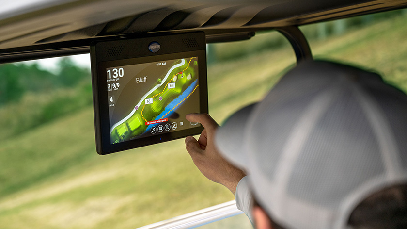 A hand reaching up to use the Pace Technology screen in an E-Z-GO golf cart.