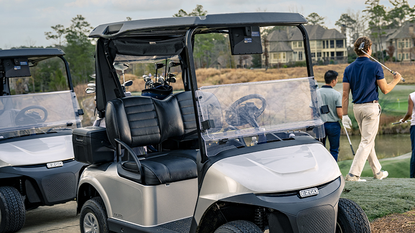 An E-Z-GO golf cart in the foreground as a golfer walks away with a golf club in hand.