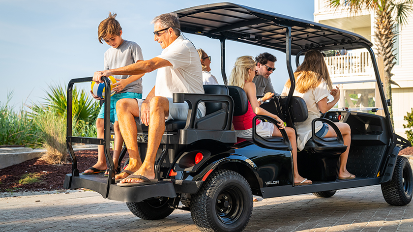 A large family of 6 sitting in an E-Z-GO Valor 6 golf cart.