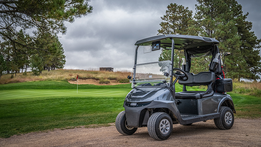 An E-Z-GO golf cart sitting next to a golf course hole.