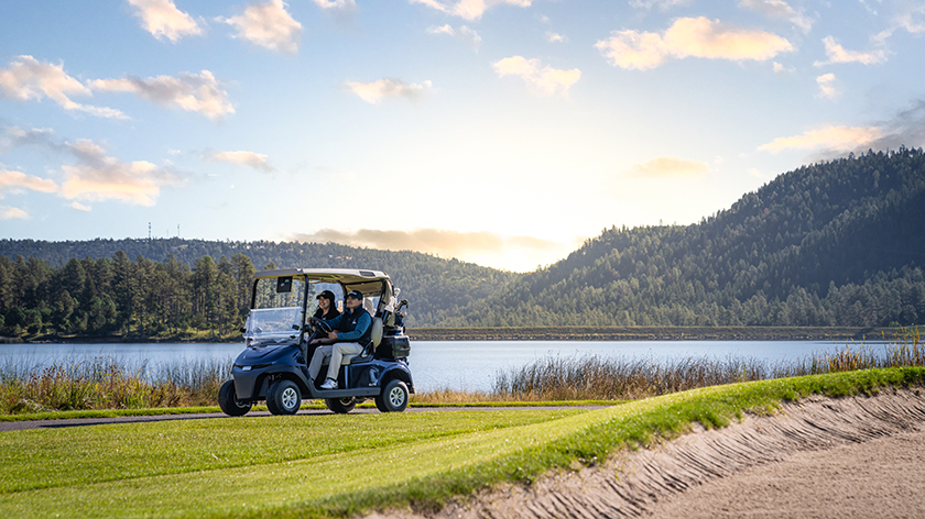 Two golfers ride their E-Z-GO golf cart alongside the water.
