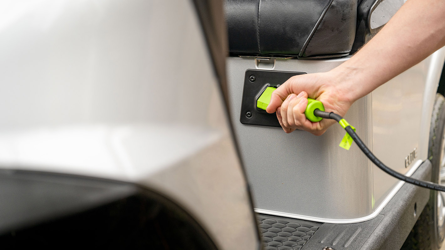 A hand inserting the ELiTE lithium charger into their E-Z-GO golf cart.
