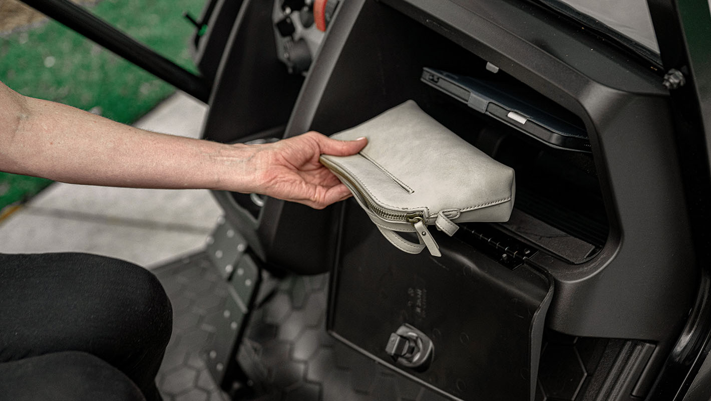 A hand putting a bag in the E-Z-GO dash compartment.