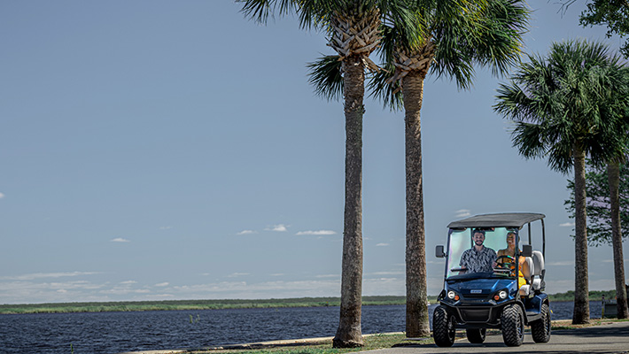 Two riders in their E-Z-GO Liberty LSV, driving down a path lined with palm trees alongside the ocean
