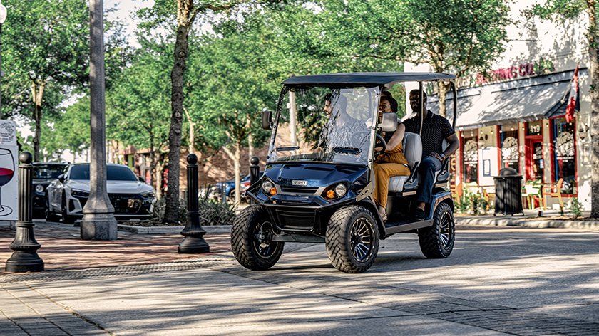 One driver and three passengers ride in an E-Z-GO Liberty LSV down a shopping street.