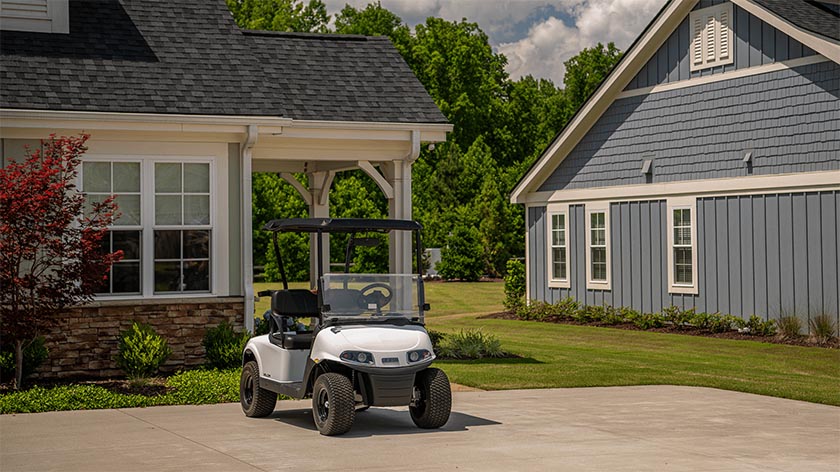 An E-Z-GO golf cart sitting empty in a driveway of a large home.