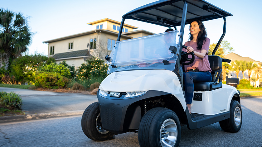 A woman driving an E-Z-GO Valor golf cart down an empty path.