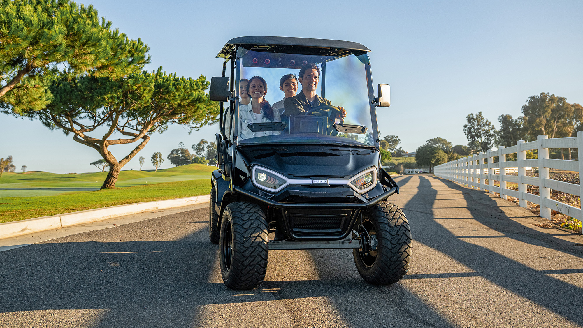 Liberty LSV with LED headlights driving a group of 4 in a neighborhood with trees, golf course and fence in background