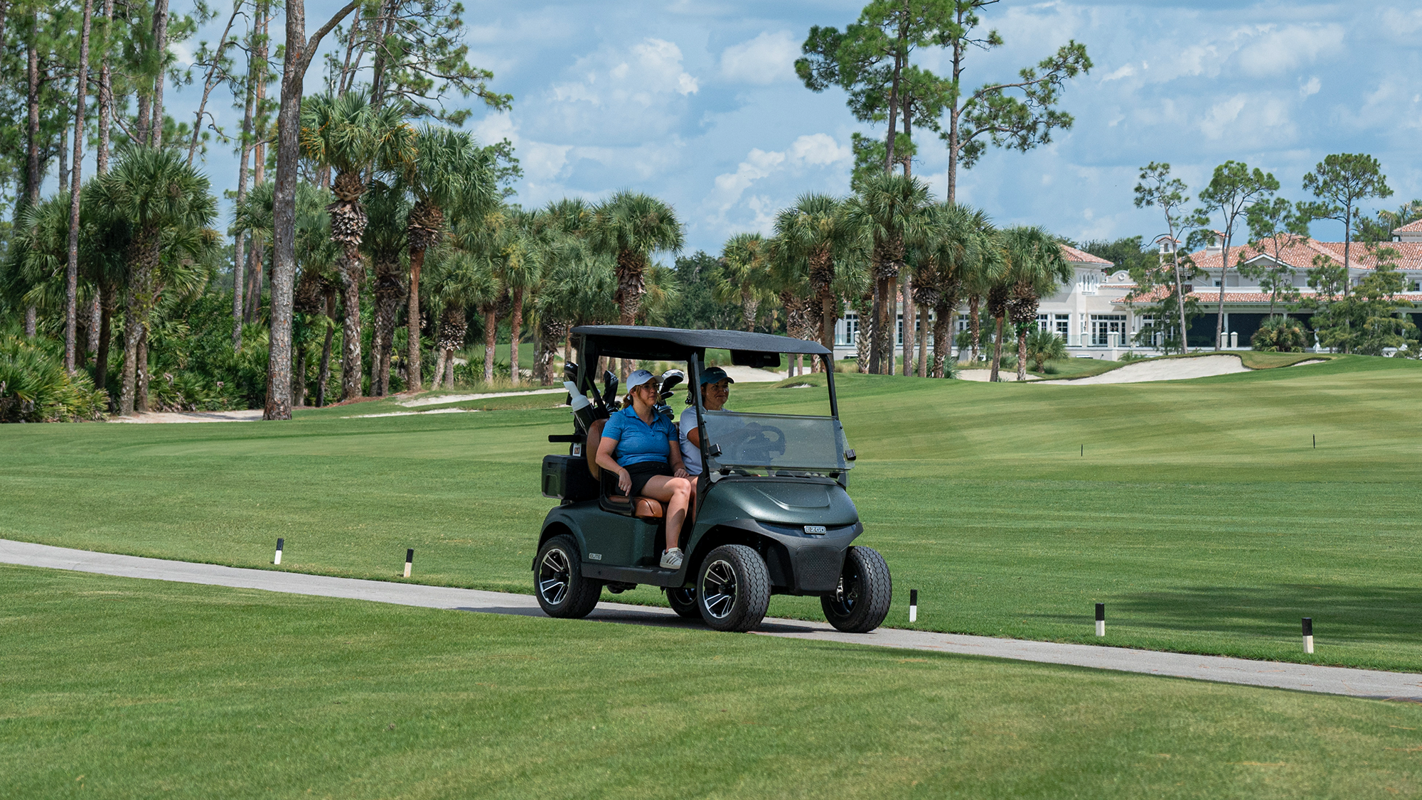 Golf cart driving on a cart path with palm trees and sand in the backgroun