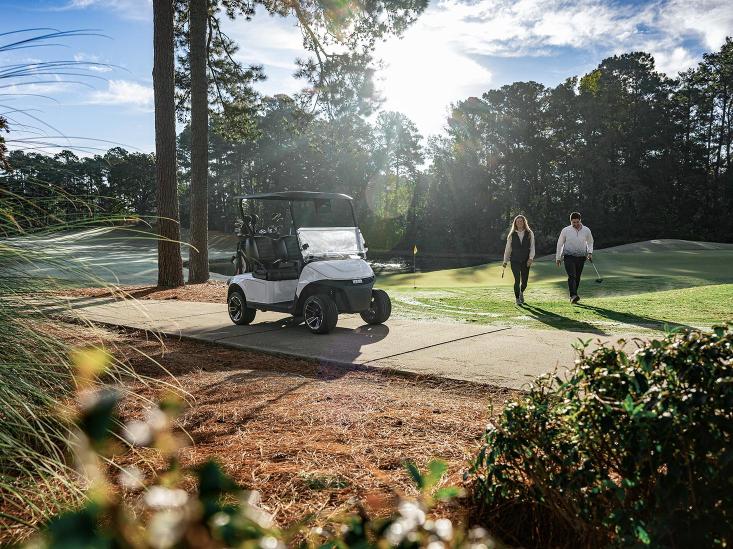 Two golfers walk toward their E-Z-GO golf cart on the golf course.