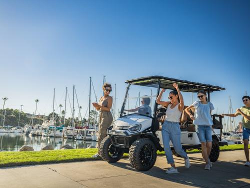 E-Z-GO Express 6 in front of a marina/harbor with sail boats in the background